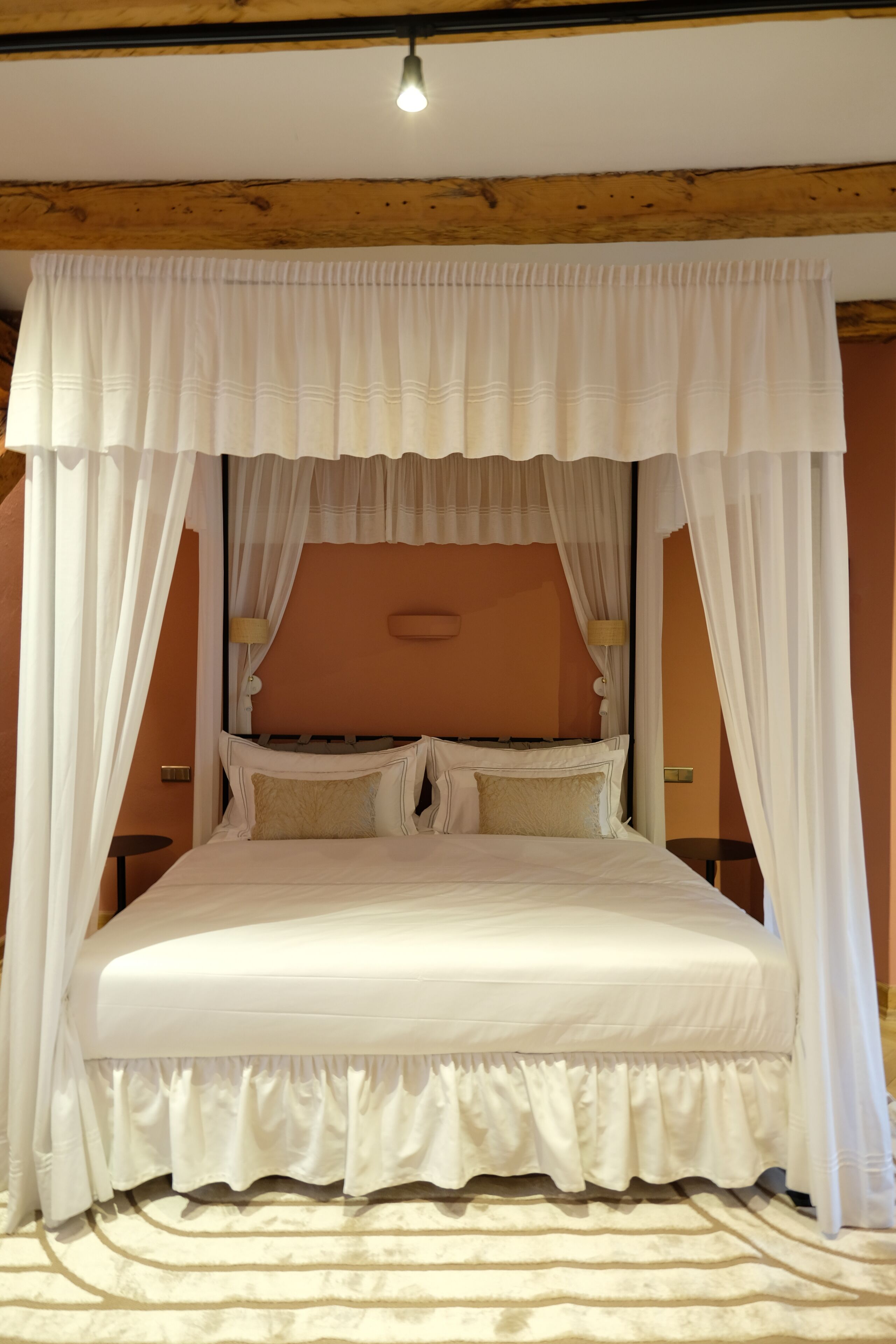 Une chambre à coucher avec un lit à baldaquin, des poutres en bois et une tête de lit dotée d’un luminaire.