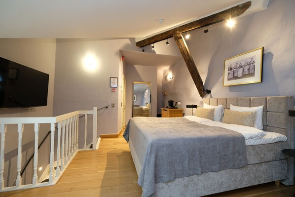 A bedroom with a large bed, a TV, a wooden staircase, and a framed picture on the wall. - The Three Sisters Hotel (Tallinn)
