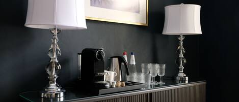 A hotel reception area with two lamps, a coffee machine, and a framed picture on the wall.
