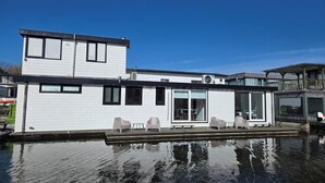 A modern houseboat with a flat roof, large windows, and a deck area with outdoor seating. - HouseBoat the NEW LAKE (Amsterdam)