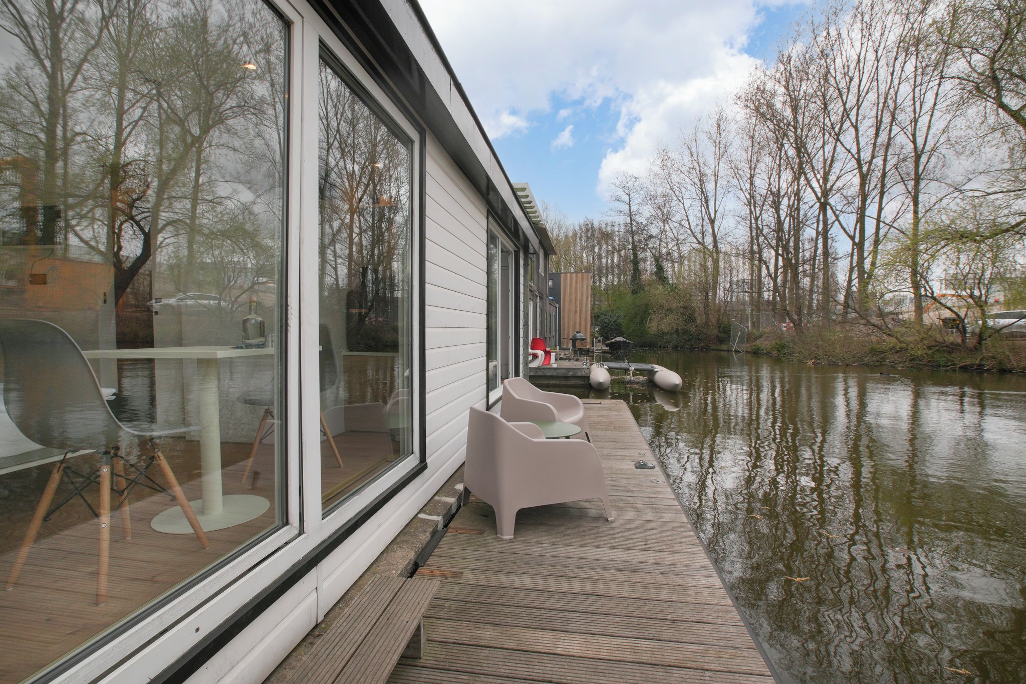 A modern house with large windows overlooking a calm water body, a wooden deck, and outdoor seating.