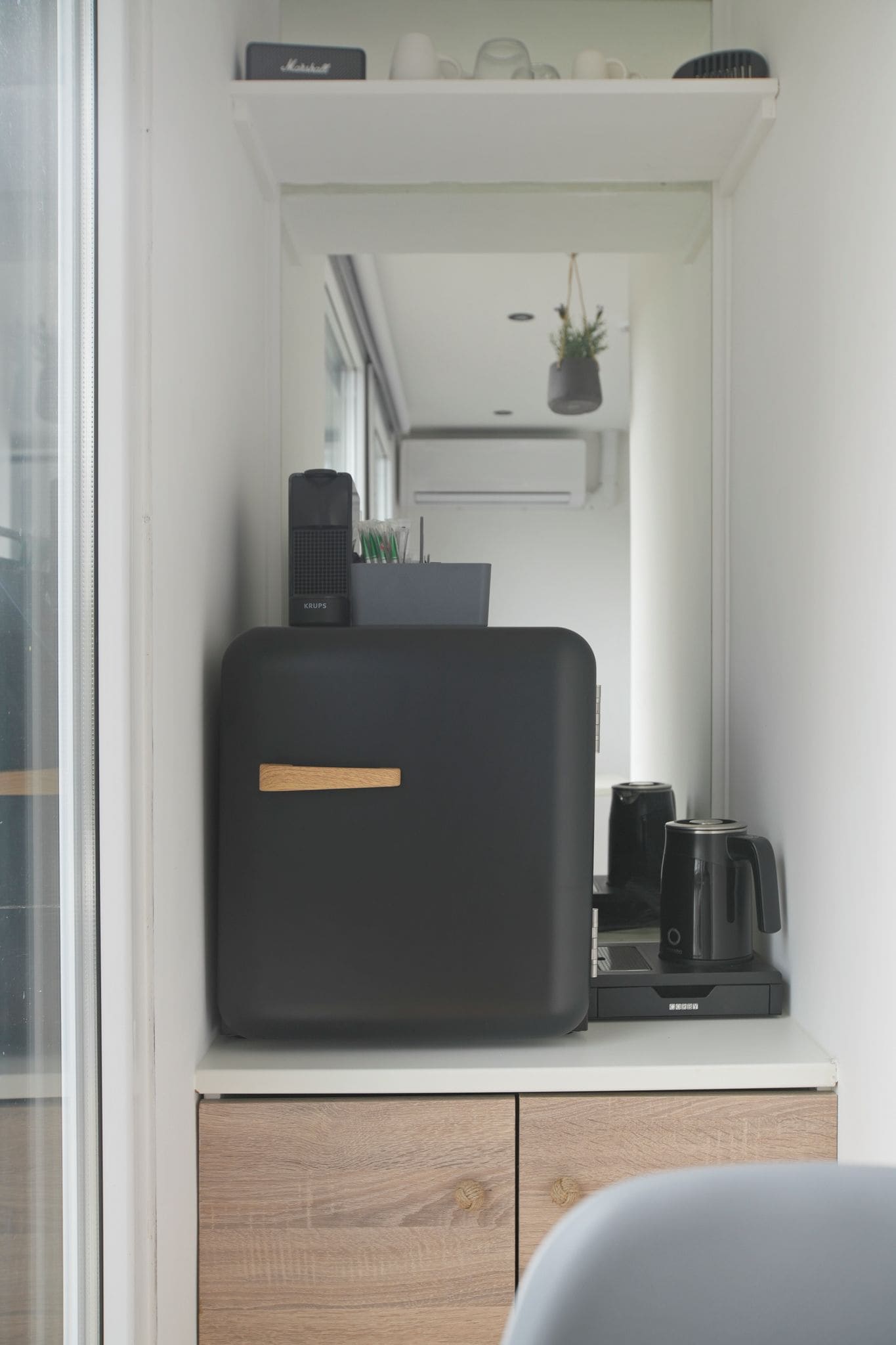 A compact kitchenette with a black appliance, a coffee maker, and a small potted plant.