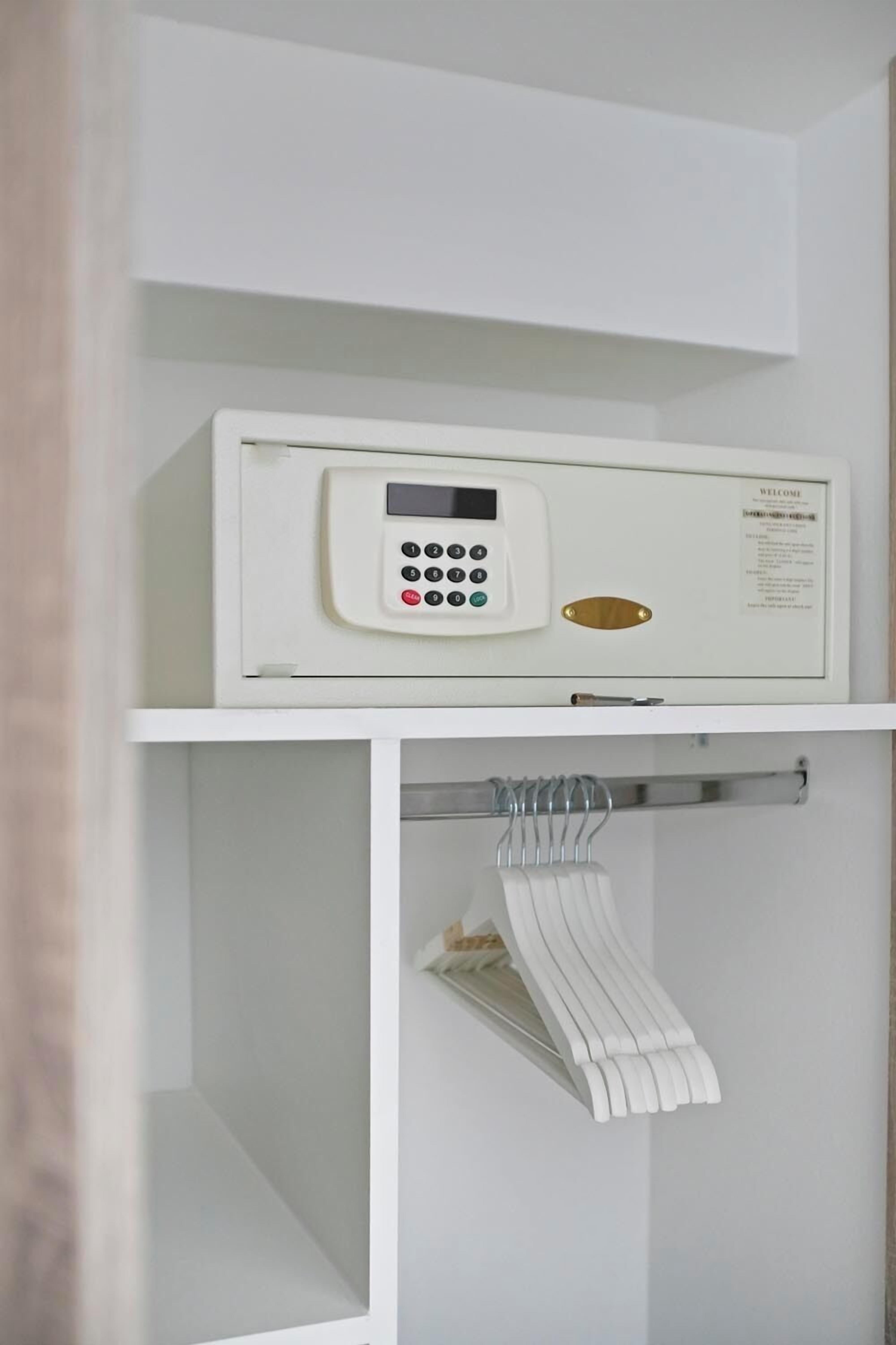 A white electronic device on a shelf, a white towel rack with towels, and a white wall.