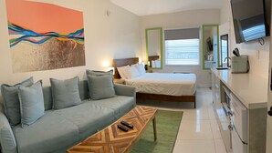 Ein modernes Hotelzimmer mit Sofa, Bett, Couchtisch aus Holz, Fernseher und Küchenzeile.