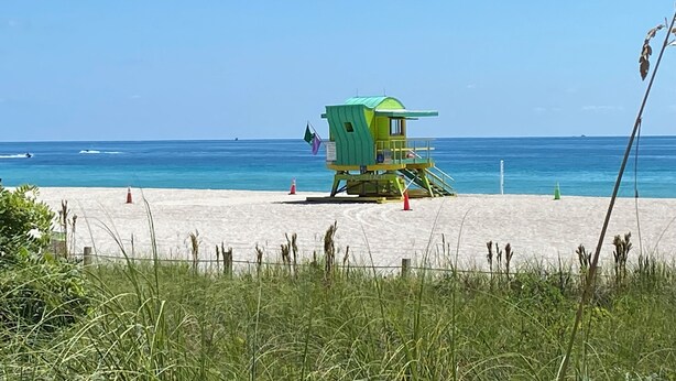 Ein Rettungsschwimmturm an einem Strand mit klarem, blauem Wasser und wolkenlosem Himmel.