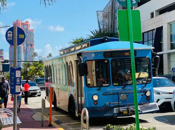 Un autobus bleu portant le numéro 32 et l’inscription « miamibeach.com » sur le côté, est garé dans une rue de la ville, avec des bâtiments et des palmiers en arrière-plan.