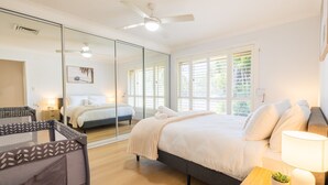 Una habitació d'hotel amb un llit gran, una tauleta de nit amb una làmpada, un ventilador de sostre i un mirall gran.