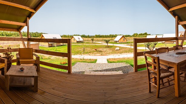 A wooden deck with a view of a rural landscape, including farm buildings and a clear sky. - Munai Sardinia (San Giovanni Suergiu)