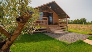 A wooden cabin with a porch, a large window, and a gravel pathway leading to the entrance. - Munai Sardinia (San Giovanni Suergiu)