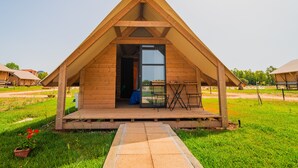 A wooden triangular structure with a glass door, a small outdoor seating area, and a concrete pathway leading to it. - Munai Sardinia (San Giovanni Suergiu)