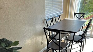 A dining area with a table and chairs, a potted plant, and a window with blinds.