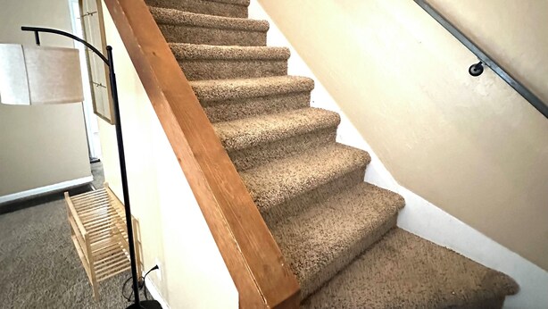 A carpeted staircase with wooden handrails and a black floor lamp.