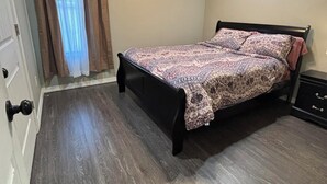 Un dormitorio con cama, ventilador de techo, ventana con cortinas y una puerta.