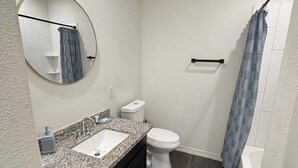 Un baño pequeño y funcional con lavamanos, inodoro y zona de ducha blancos.
