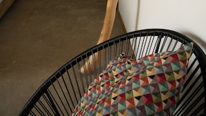 Une pièce avec un mur de couleur turquoise, une décoration en forme de branche d'arbre, une chaise en fil de fer noir avec un coussin coloré, et un lit avec une literie blanche.