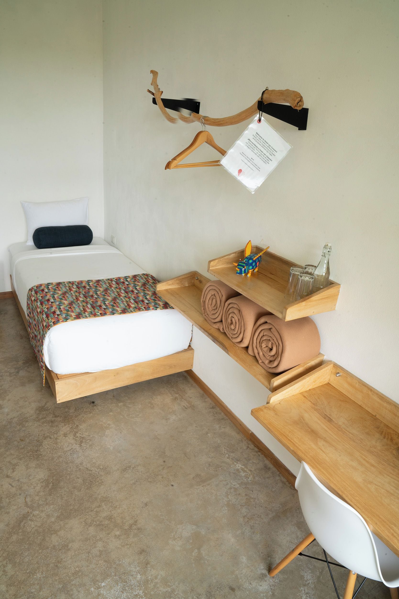 A bedroom with a bed, a wooden desk, a chair, and a wall-mounted hanger with a tag.