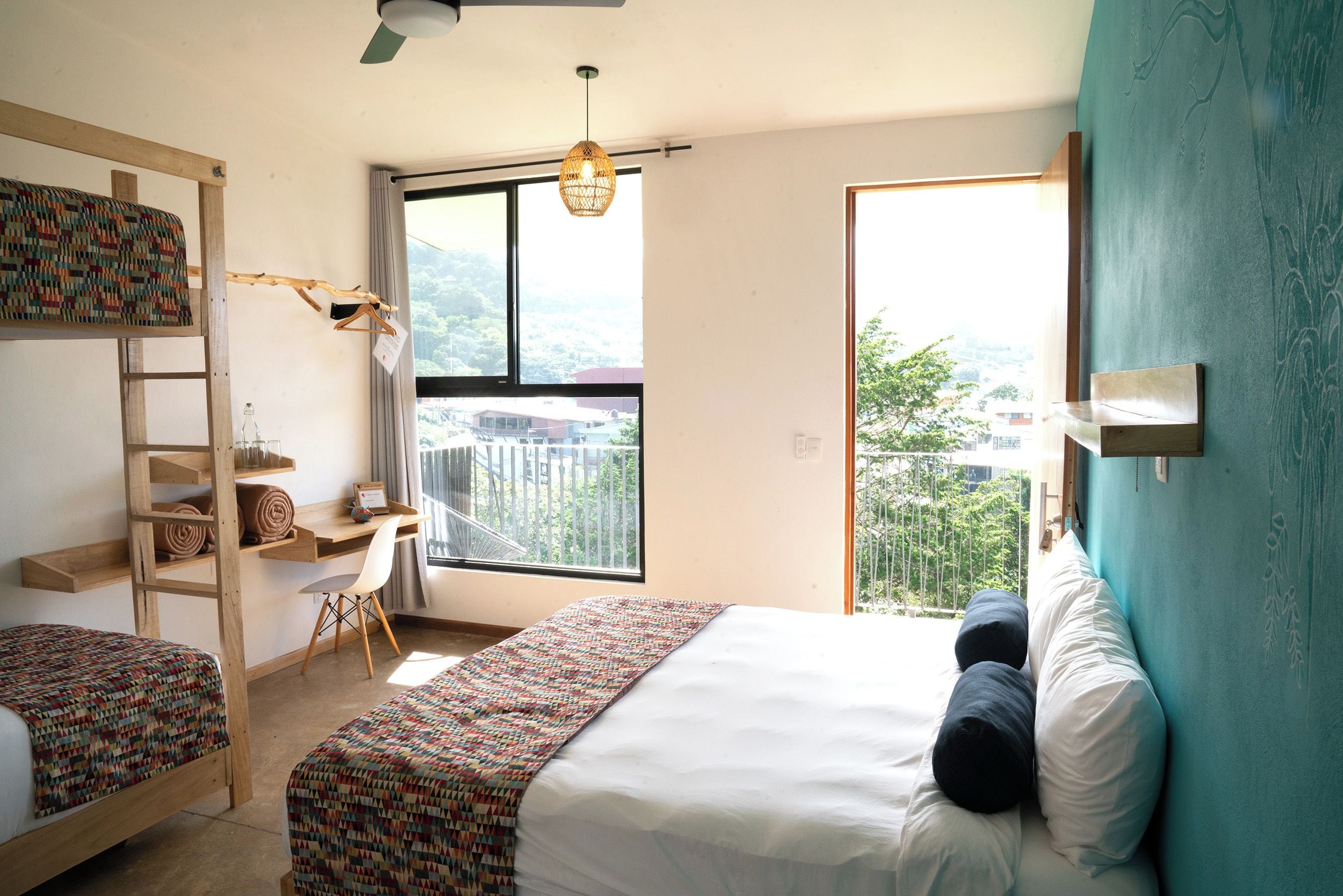 A bedroom with a bunk bed, a desk, and a large window with a view.