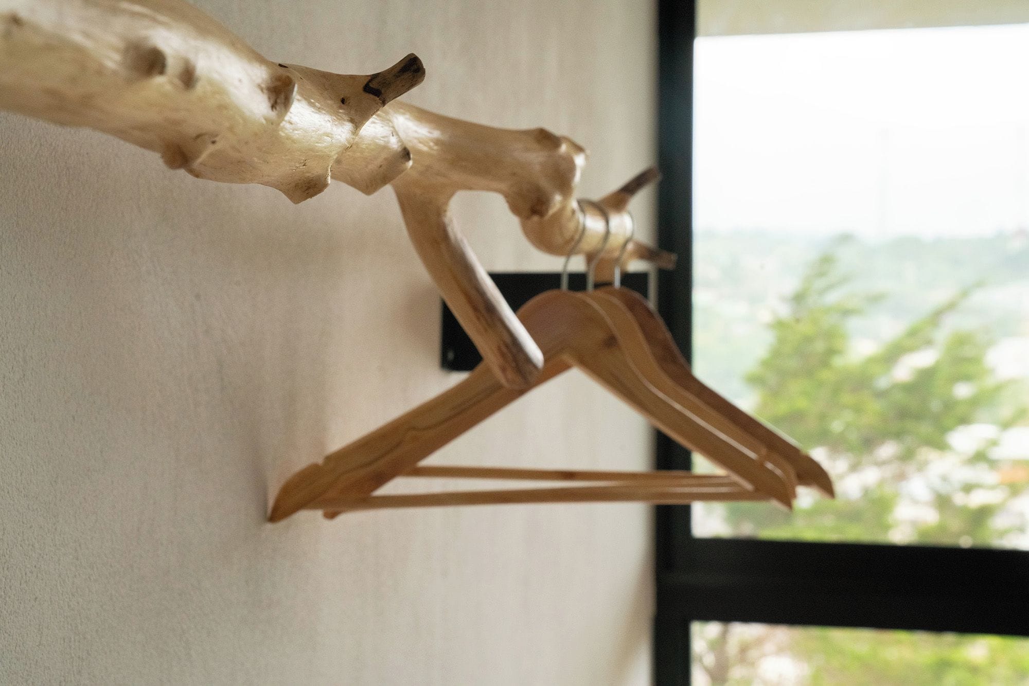 A wooden coat rack with a coat hanger and a wooden hanger against a wall.