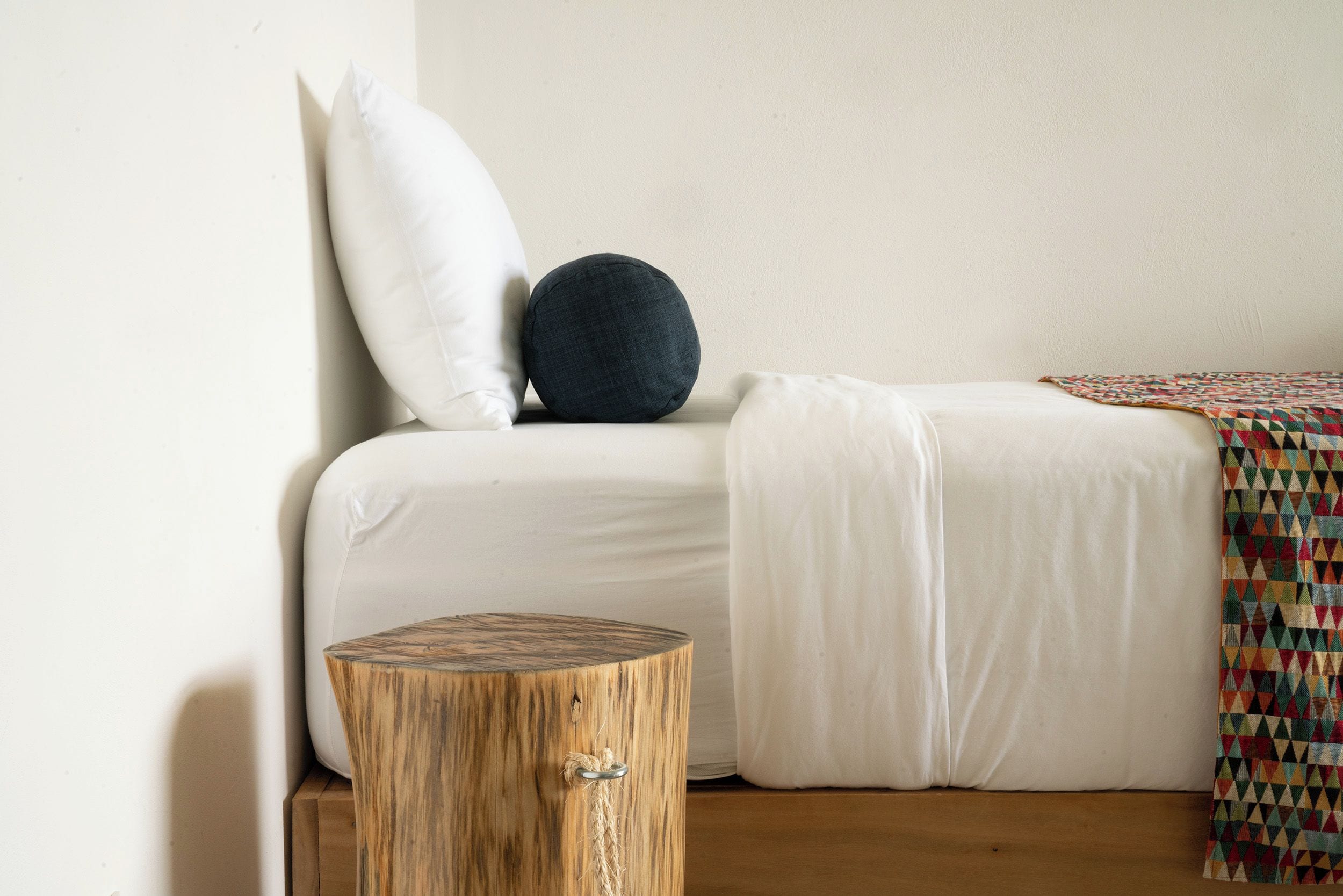 A bed with white bedding, a dark round pillow, and a patterned blanket.