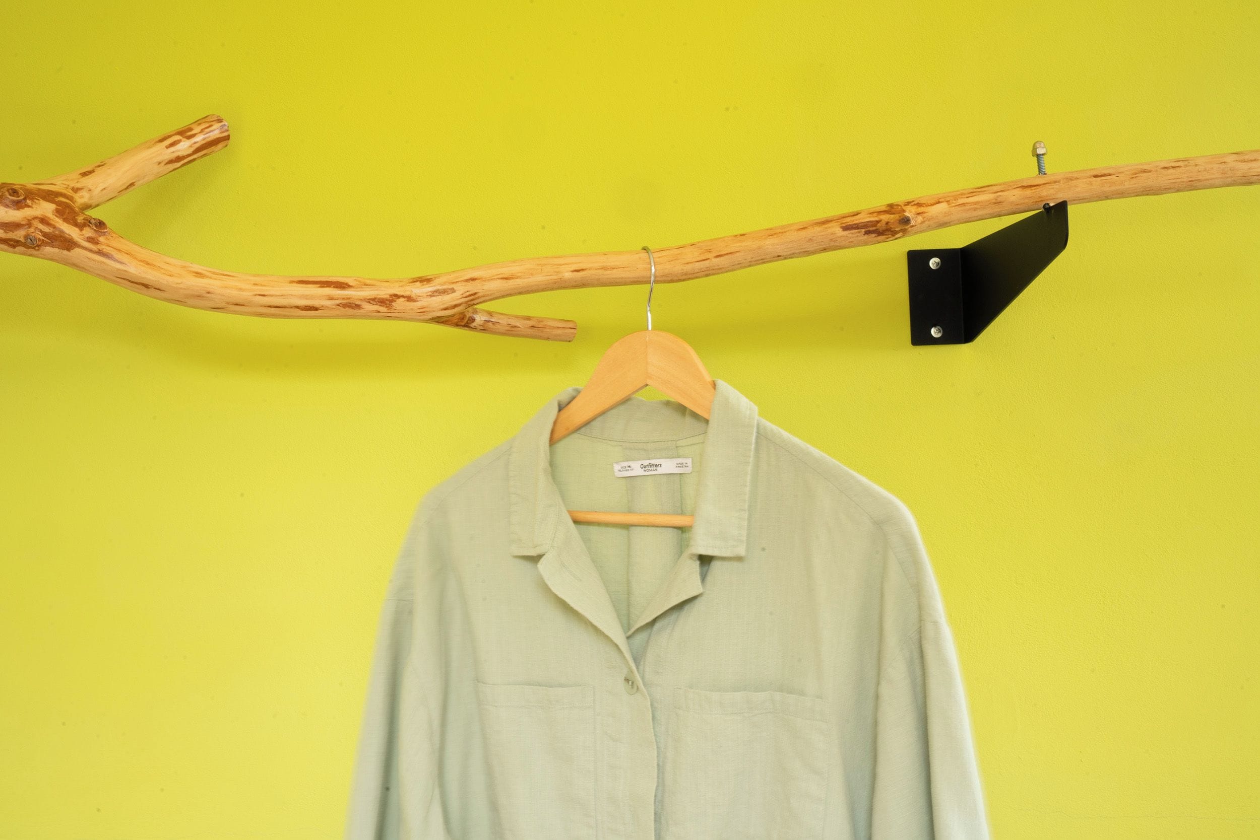 A light-colored shirt hanging on a wooden hanger against a yellow wall.
