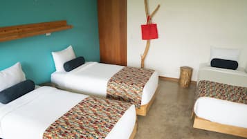 A room with two single beds, a small table, and a red bag hanging on a branch.