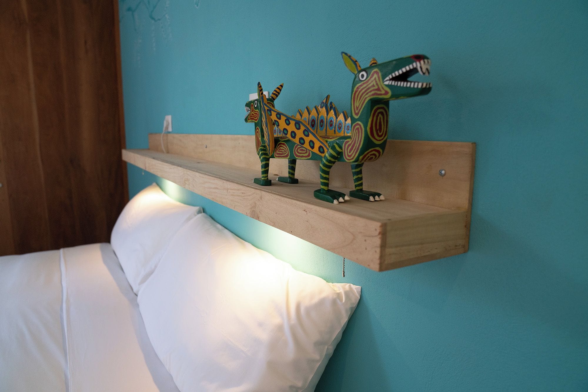 A bed with white bedding and a wooden shelf with colorful dinosaur figures.