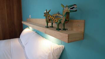 Una cama con ropa blanca y un estante de madera con figuras de dinosaurios de colores.