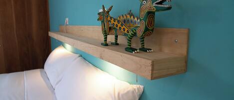 A bed with white bedding and a wooden shelf with colorful dinosaur figures.