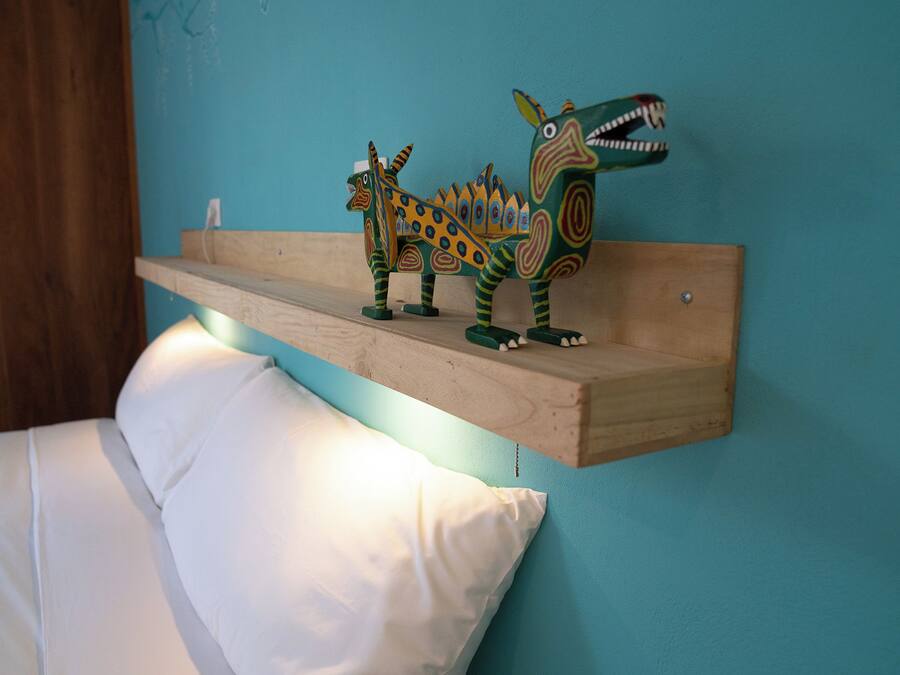 Una cama con ropa blanca y un estante de madera con figuras de dinosaurios de colores.