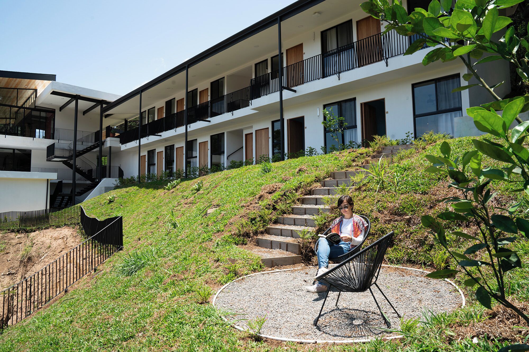 A modern building with a staircase leading to a flat-roofed area with a seating area and a garden.