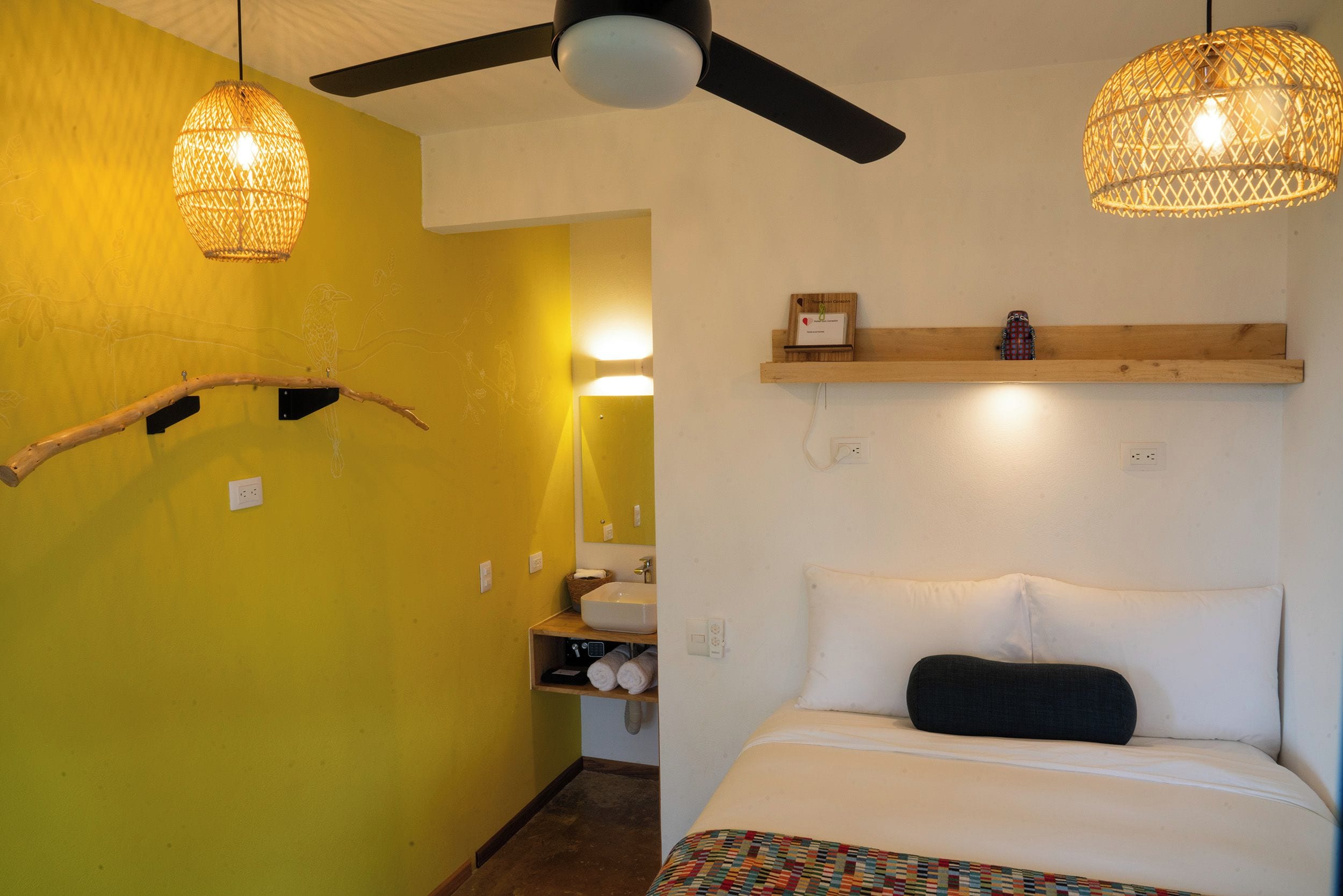 Une pièce avec un lit, un ventilateur de plafond et deux lampes suspendues.