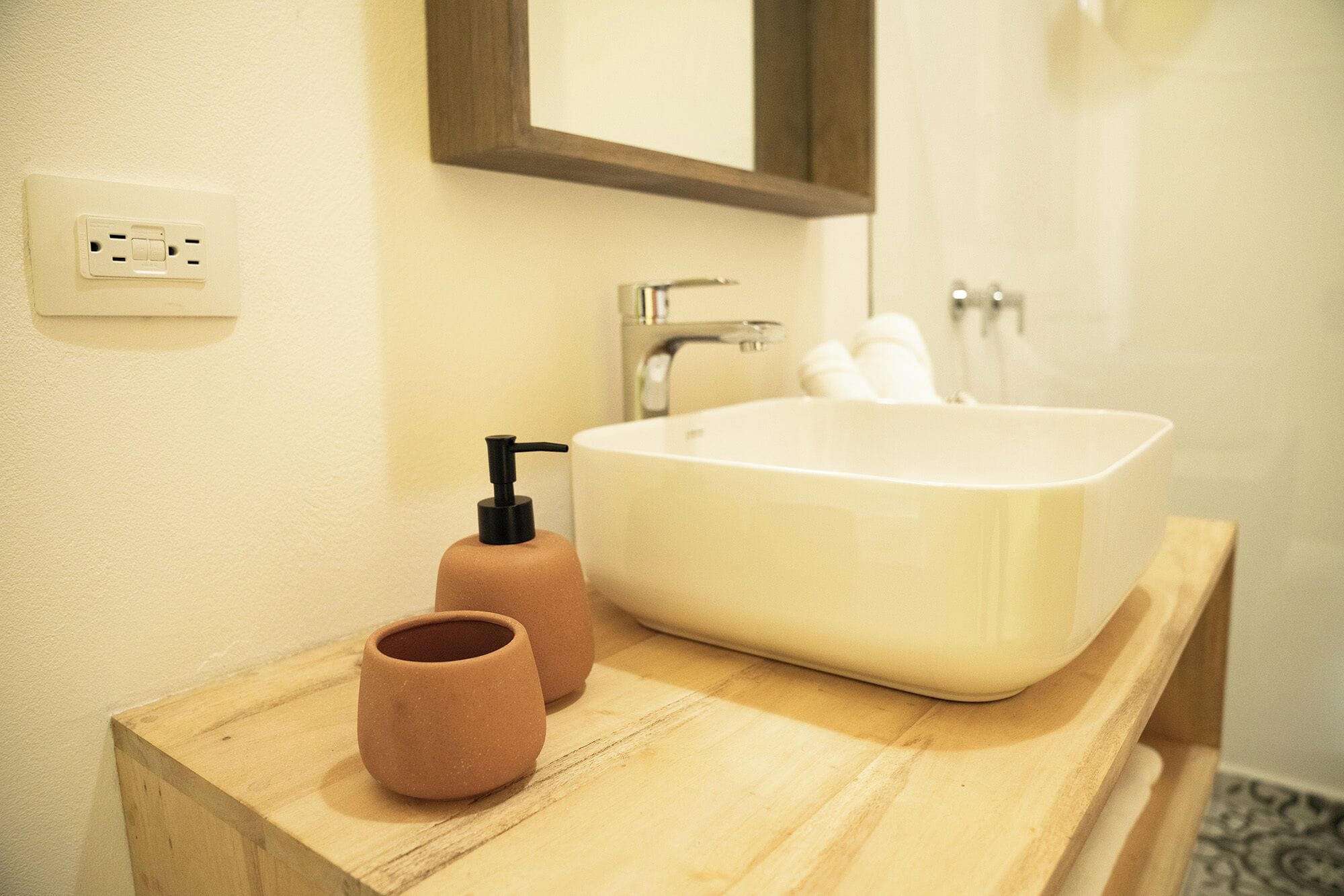 Un baño con un lavabo blanco, un mueble de tocador de madera, un espejo y una botella de jabón.
