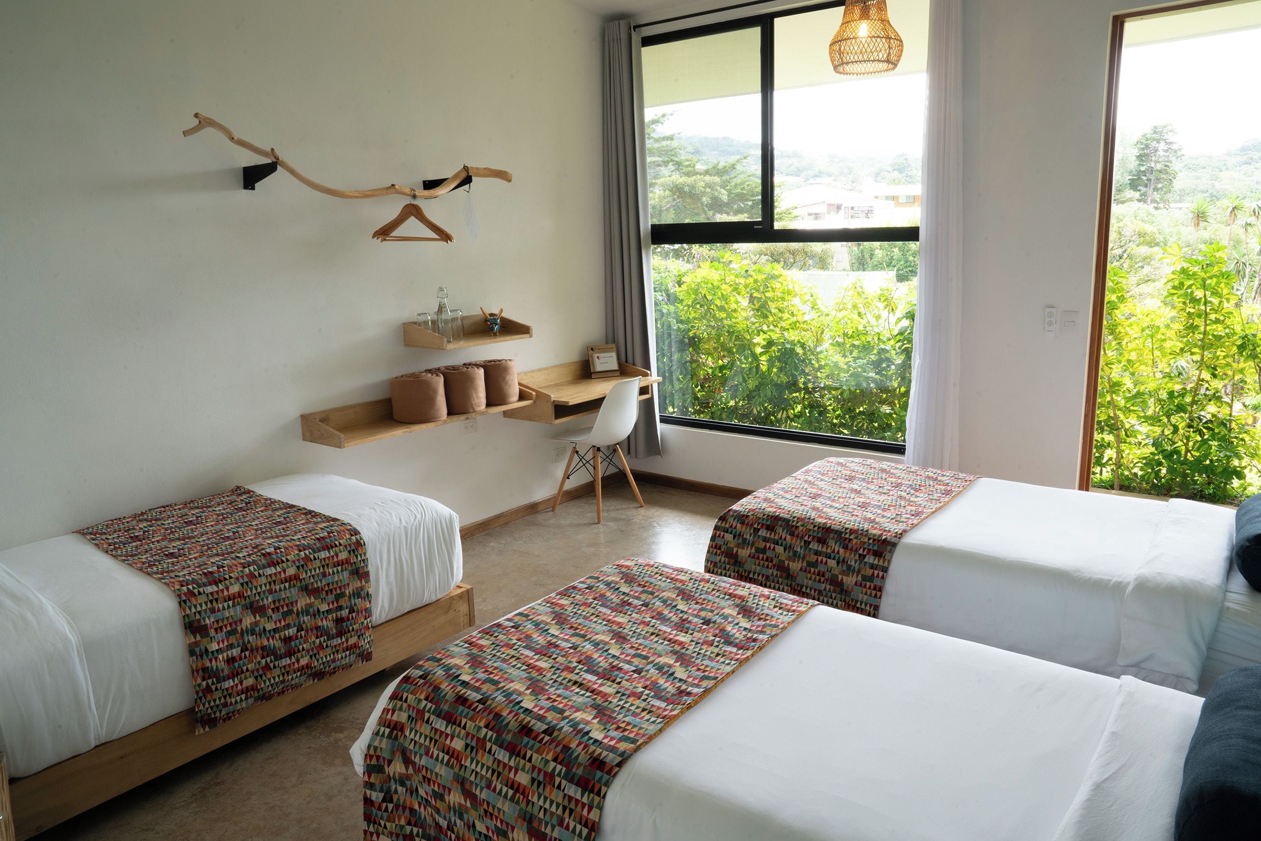 Habitación de hotel con dos camas, un escritorio y una ventana con vista a follaje.