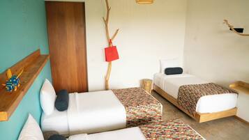 A room with two beds, a wooden shelf, a wall-mounted branch, and a hanging red bag.