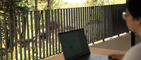A person using a laptop at a table with a view of trees through a fence.