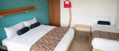 A hotel room with a bed, a smaller bed, a wooden headboard, a wall art piece, a hanging light fixture, and a small table.