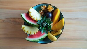 Un panier de fruits contenant des tranches de pastèque, d’ananas, de mangue et de banane, ainsi qu’une prune, posé sur une table en bois.