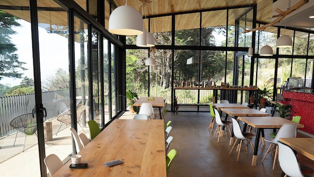 Un espace de restauration intérieur avec des tables et des chaises en bois, de grandes fenêtres et des lampes suspendues.