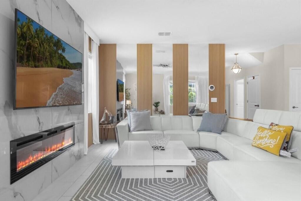 Una sala de estar moderna con chimenea, sofás blancos, una mesa de centro y un televisor grande montado en la pared.