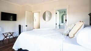 A bedroom with a large bed, a flat-screen TV mounted on the wall, and a door leading to a bathroom.