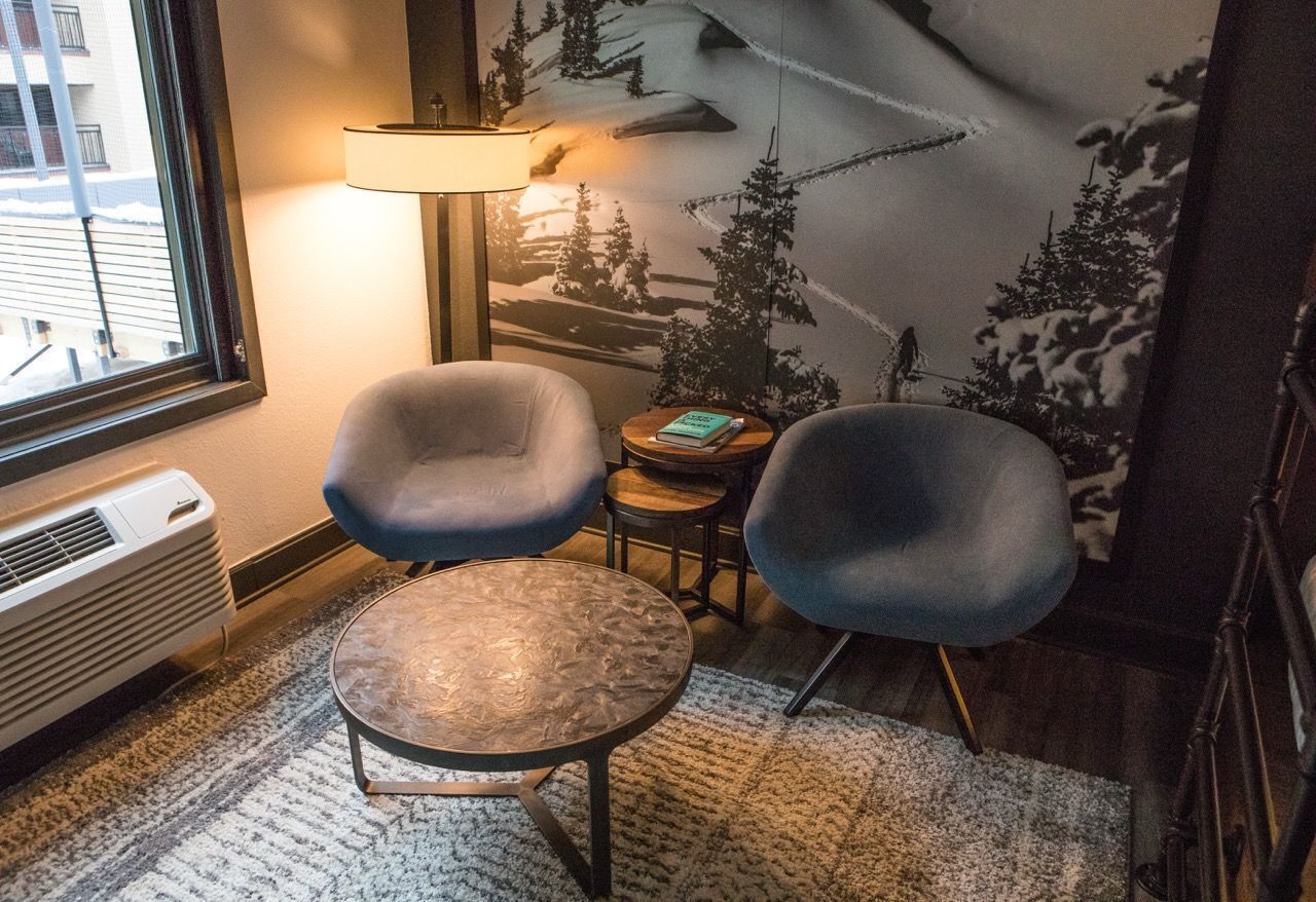 Une pièce chaleureuse avec deux fauteuils, une petite table ronde, une lampe et une fresque murale représentant un paysage enneigé.