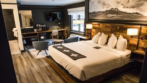 Habitación de hotel con una cama grande, un escritorio con silla, televisor, baño y vistas a la montaña.