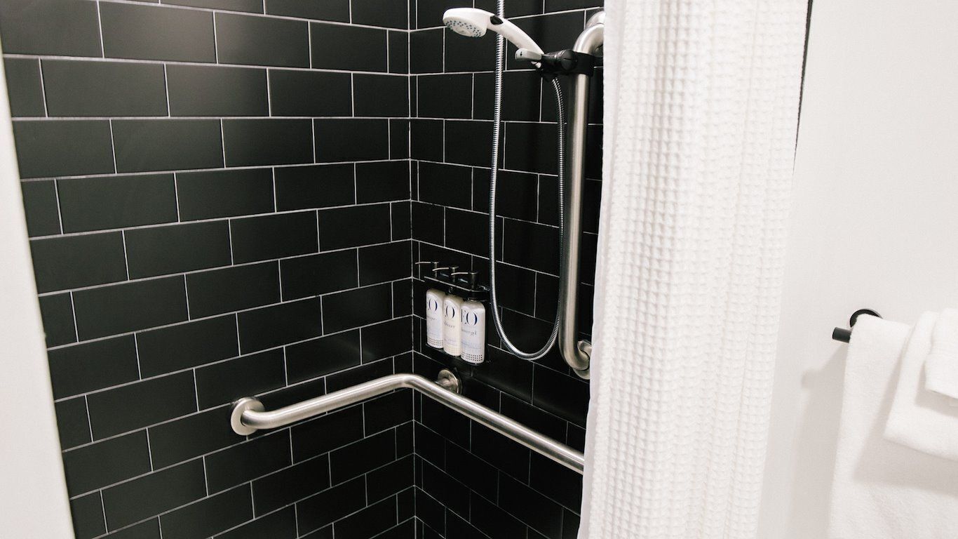 A bathroom with black tiled walls, a white towel, and a shower with a handheld showerhead.