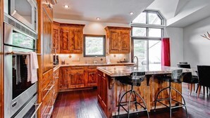 Una cocina moderna con armarios de madera, una isla central con taburetes y un amplio ventanal que proporciona luz natural.