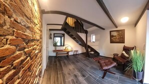 A room with a brick wall, a wooden bench, a brown leather chair, a staircase, and a framed picture on the wall. - Anno 1895 - Holiday home for up to 4 people, pets welcome (Manslagt)