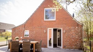 A brick house with a patio, a dining table with chairs, and a sliding glass door. - Anno 1895 - Holiday home for up to 4 people, pets welcome (Manslagt)