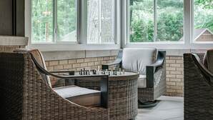 Ein gemütliches Zimmer mit Korbmöbeln, einem Kicker und großen Fenstern mit Blick auf Grünflächen.