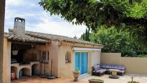 A patio with a tiled floor, a built-in kitchen area, a seating area with a sofa and a table, and potted plants.