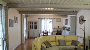 A living room with a yellow sofa, a dining table with chairs, and a kitchen area with cabinets and a radiator.
