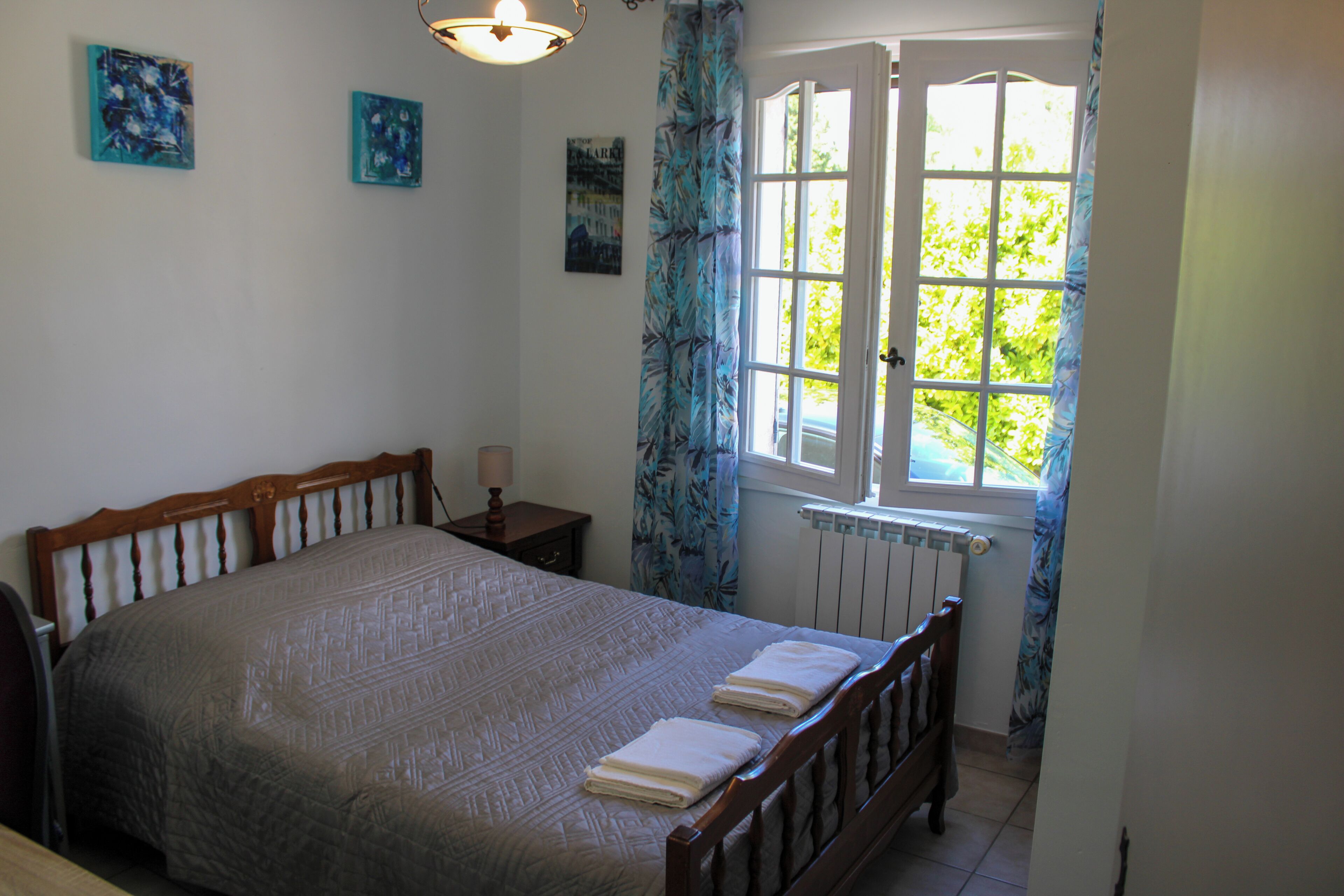 Une chambre à coucher avec un grand lit, une table de chevet, une fenêtre avec des rideaux et des œuvres d’art murales.